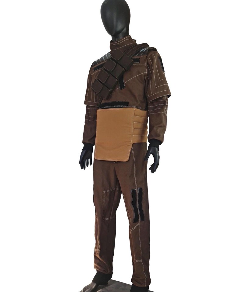 Puede incluir: Un disfraz marr&oacute;n exhibido en un maniqu&iacute;. El atuendo incluye una chaqueta de cuello alto con costuras blancas, una pieza para el pecho y pantalones a juego. Guantes y botas negras completan el conjunto. El disfraz tiene una est&eacute;tica futurista o militar.