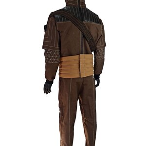 Puede incluir: Un disfraz marr&oacute;n exhibido en un maniqu&iacute;. El atuendo incluye una chaqueta con costuras blancas y un cintur&oacute;n color canela. El disfraz tambi&eacute;n presenta pantalones a juego y una correa para el hombro. El maniqu&iacute; tiene una cabeza negra y guantes negros.