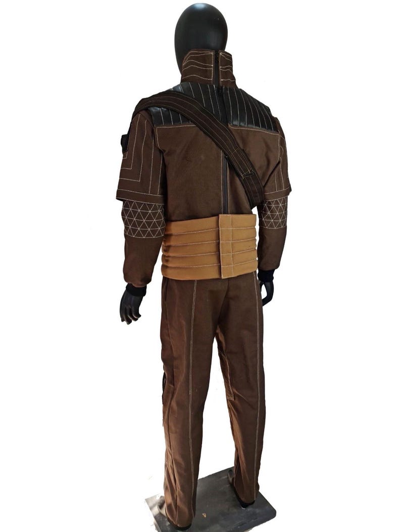 Puede incluir: Un disfraz marr&oacute;n exhibido en un maniqu&iacute;. El atuendo incluye una chaqueta con costuras blancas y un cintur&oacute;n color canela. El disfraz tambi&eacute;n presenta pantalones a juego y una correa para el hombro. El maniqu&iacute; tiene una cabeza negra y guantes negros.