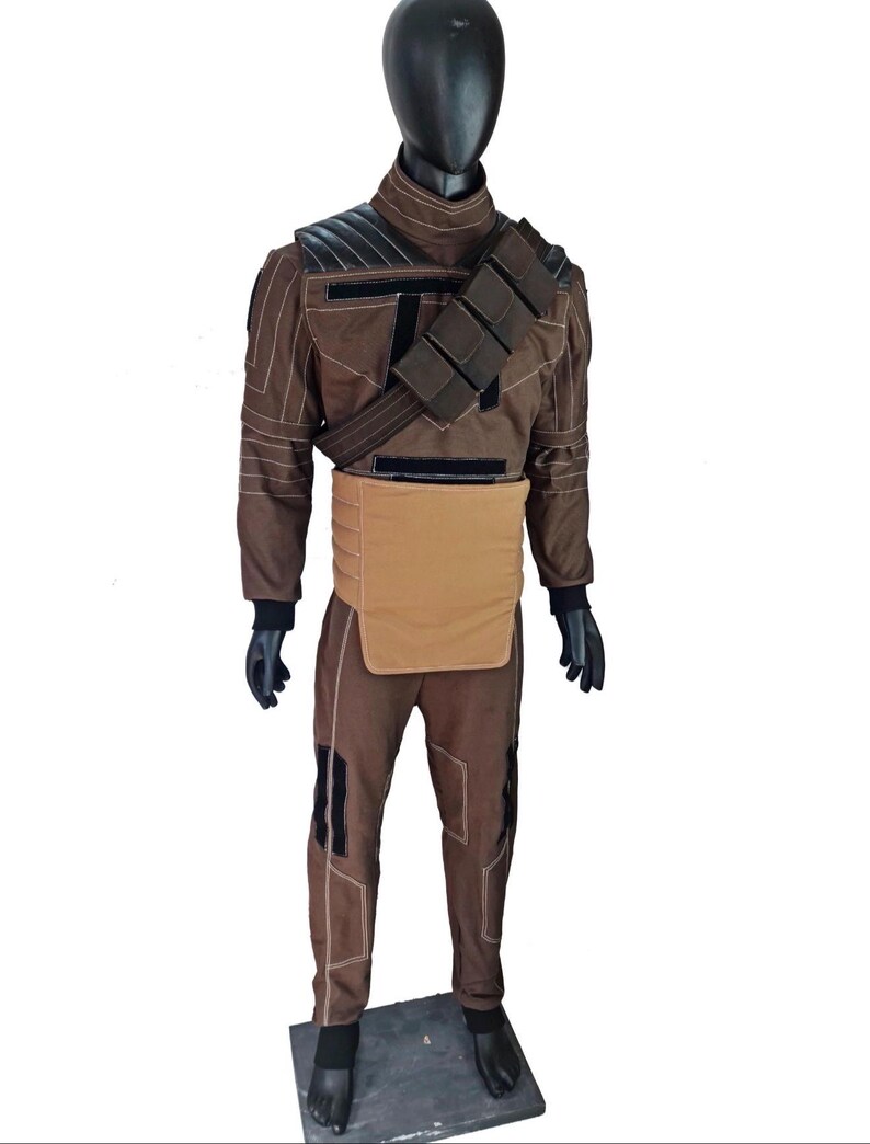 Puede incluir: Traje marr&oacute;n con detalles negros, exhibido en un maniqu&iacute;. El atuendo incluye una chaqueta de manga larga, pantalones y una pieza para el pecho. La chaqueta tiene un cuello alto y acolchado en los hombros. El disfraz tambi&eacute;n presenta un cintur&oacute;n con bolsas y guantes negros.
