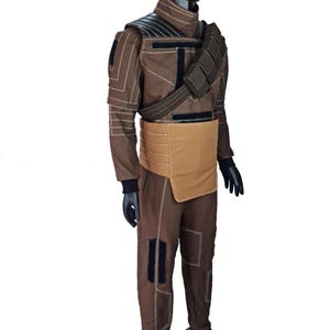 Puede incluir: Un disfraz marr&oacute;n con detalles en negro, exhibido en un maniqu&iacute;. El atuendo incluye una chaqueta con protecci&oacute;n para los hombros, pantalones y un cintur&oacute;n con una bolsa. El disfraz tiene costuras blancas y guantes negros.