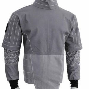 Puede incluir: Chaqueta gris con costuras blancas. Cuello alto, mangas cortas con patrones geom&eacute;tricos y dise&ntilde;o bicolor. Pu&ntilde;os negros. Peque&ntilde;o parche negro en el hombro izquierdo.