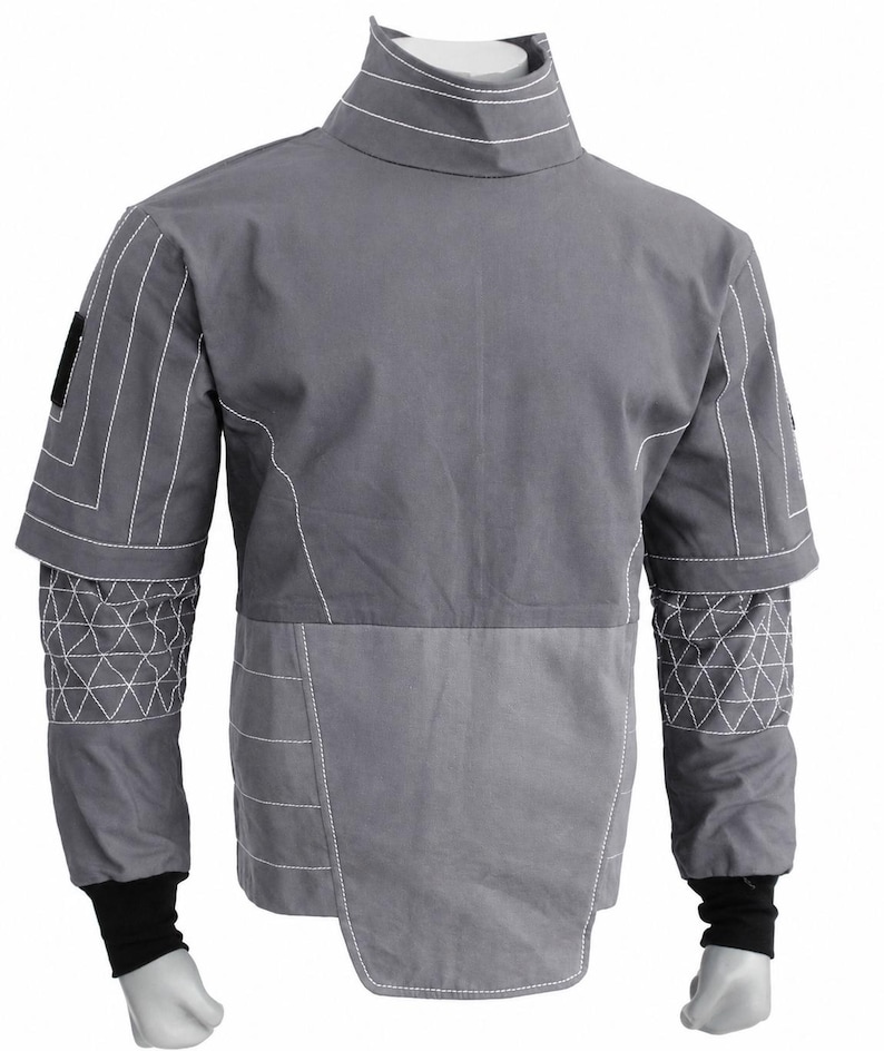 Puede incluir: Chaqueta gris con costuras blancas. Cuello alto, mangas cortas con patrones geom&eacute;tricos y dise&ntilde;o bicolor. Pu&ntilde;os negros. Peque&ntilde;o parche negro en el hombro izquierdo.