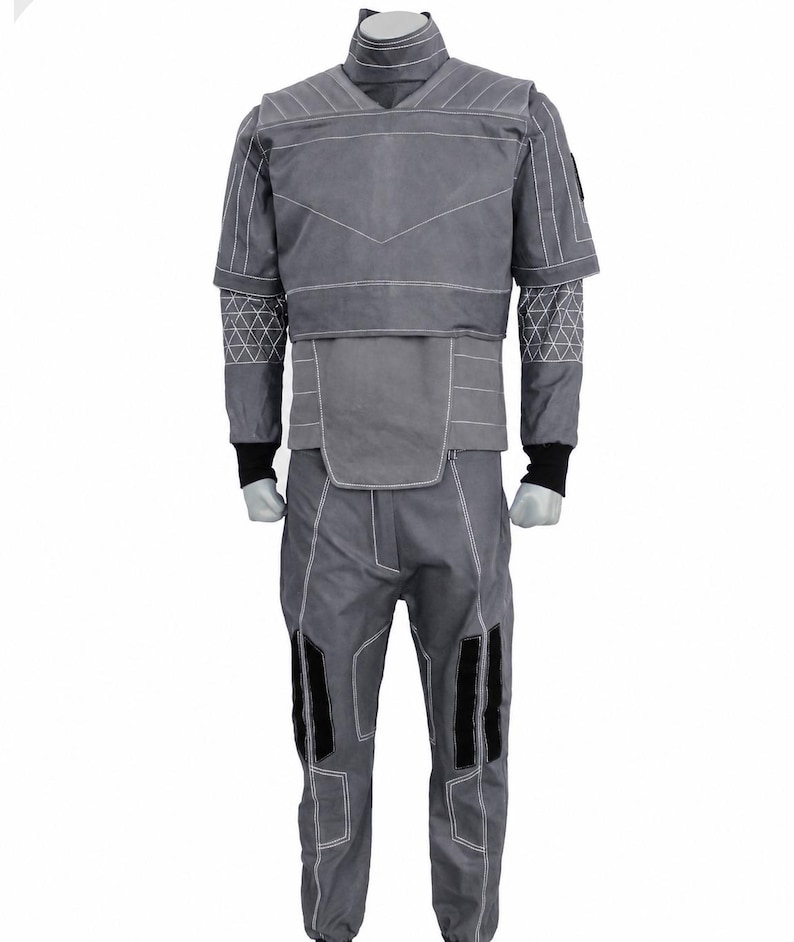 Puede incluir: Mono gris con costuras blancas y detalles negros. El traje presenta un cuello alto, mangas cortas y patrones geom&eacute;tricos en los brazos. Los pantalones tienen rodilleras negras. El dise&ntilde;o sugiere un tema futurista o t&aacute;ctico.