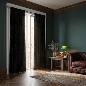 Peut inclure: Intérieur d'une pièce avec des rideaux en velours noir devant une fenêtre. La pièce comprend des murs vert foncé, un canapé en cuir marron, une table d'appoint en bois et une lampe verte.