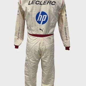 May include: A white racing suit featuring the name LECLERC in black text, a blue HP logo, a black Puma logo, and a Ferrari emblem on the collar. The suit includes red accents on the collar and waist, with Richard Mille text on the sleeves.
