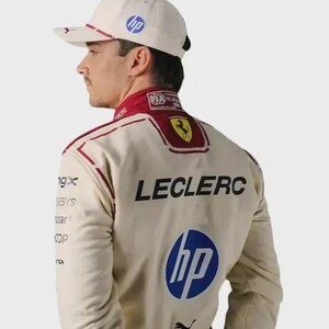 May include: A beige racing suit and matching baseball cap featuring the name LECLERC in black lettering, a blue HP logo, a yellow Ferrari emblem, and a black Puma logo. The suit includes red accents and various sponsor logos on the sleeves.