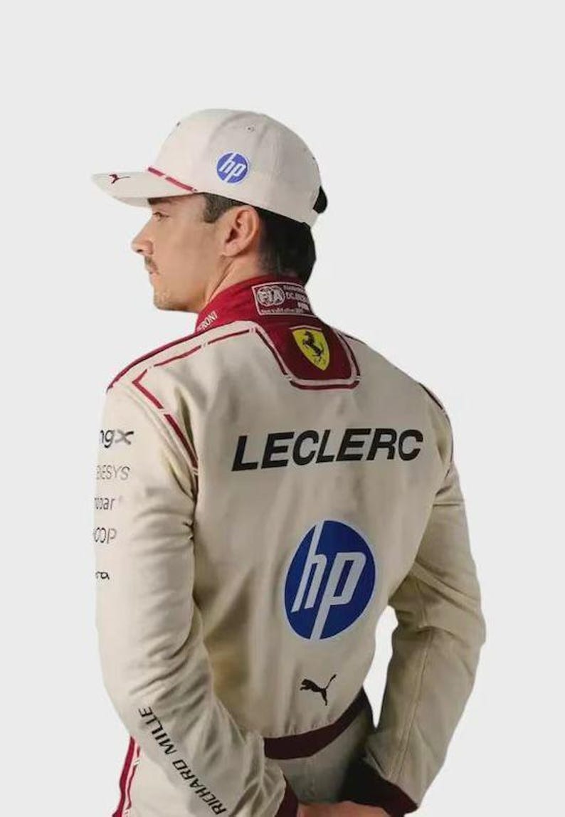 May include: A beige racing suit and matching baseball cap featuring the name LECLERC in black lettering, a blue HP logo, a yellow Ferrari emblem, and a black Puma logo. The suit includes red accents and various sponsor logos on the sleeves.