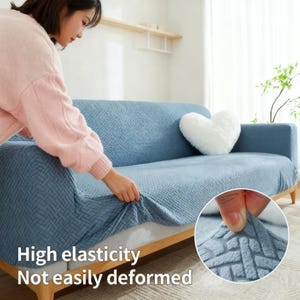 May include: A light blue sofa cover with a textured pattern is being stretched over a sofa. The cover is being installed by a person. The text "High elasticity, Not easily deformed" is visible.