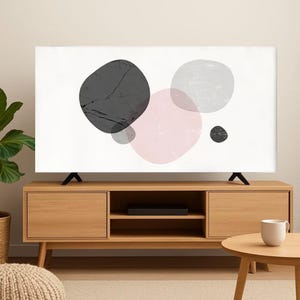 Può includere: Una copertura TV bianca con un design astratto di forme sovrapposte in nero, grigio e rosa. La copertura è su un mobile TV in legno dal design moderno. Sono visibili anche un tavolino rotondo e una pianta.