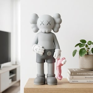K&ouml;nnte beinhalten: Eine graue KAWS-Figur mit totenkopfartigem Kopf, X-f&ouml;rmigen Augen und wei&szlig;en Handschuhen, die eine dunkelgraue Shorts tr&auml;gt. Die Figur h&auml;lt einen kleinen rosa KAWS-Begleiter an der Hand. Die Figur hat eine glatte, matte Oberfl&auml;che und steht aufrecht.