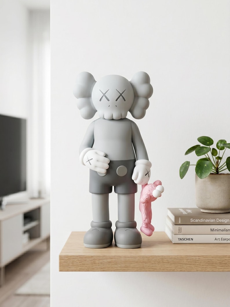 K&ouml;nnte beinhalten: Eine graue KAWS-Figur mit totenkopfartigem Kopf, X-f&ouml;rmigen Augen und wei&szlig;en Handschuhen, die eine dunkelgraue Shorts tr&auml;gt. Die Figur h&auml;lt einen kleinen rosa KAWS-Begleiter an der Hand. Die Figur hat eine glatte, matte Oberfl&auml;che und steht aufrecht.