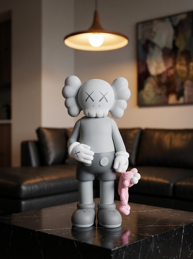 K&ouml;nnte beinhalten: Eine graue Vinyl-Sammelfigur mit einem totenkopfartigen Kopf, X-f&ouml;rmigen Augen, abgerundeten Ohren und wei&szlig;en Handschuhen. Die Figur tr&auml;gt eine dunkelgraue Shorts und h&auml;lt eine kleine, rosa, pl&uuml;schartige Figur in ihrer linken Hand.