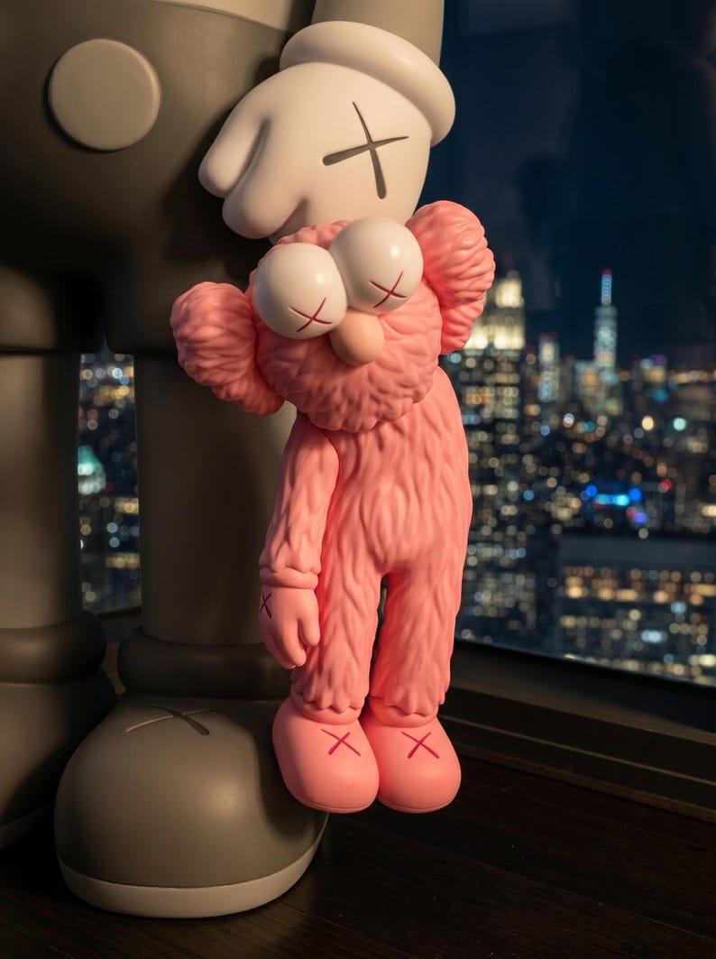 K&ouml;nnte beinhalten: Eine rosafarbene, flauschige, anthropomorphe Figur mit gro&szlig;en, runden Augen und X-f&ouml;rmigen Pupillen, die an der Hand einer gr&ouml;&szlig;eren, grauen Figur mit glatter Oberfl&auml;che h&auml;ngt. Beide Figuren haben X-f&ouml;rmige Markierungen an H&auml;nden und F&uuml;&szlig;en.