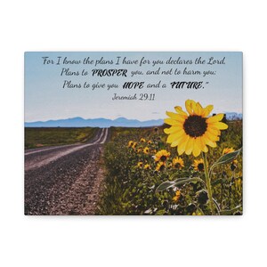 May include: Canvas art print featuring a scenic landscape with a gravel road leading to distant mountains. A field of sunflowers in full bloom is in the foreground. The text reads: "For I know the plans I have for you...Jeremiah 29:11."