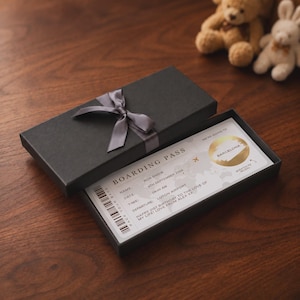 May include: A black rectangular gift box with a grey satin ribbon bow, containing a boarding pass with the text "BOARDING PASS", "BARCELONA", "BOB SNOW", "4TH SEPTEMBER 2026", "08:00 AM", "LUTON AIRPORT", and "HAPPY 21ST BIRTHDAY TO THE LOVE OF MY LIFE!"