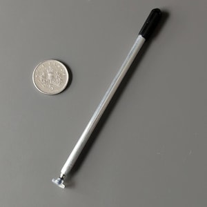 Op de afbeelding: Een dunne, zilverkleurige metalen stylus met een zwarte dop aan het ene uiteinde en een kleine, doorzichtige plastic schijfpunt aan het andere uiteinde, naast een zilveren munt. De tekst RETROPOINT UK met een blauw cursorpictogram is zichtbaar.