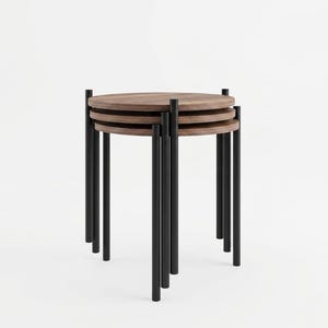 Puede incluir: Un juego de tres mesas nido con tableros circulares de madera veteada en color marrón oscuro y patas delgadas de metal negro. Las mesas están apiladas verticalmente, cada una sostenida por tres patas cilíndricas que sobresalen del tablero.