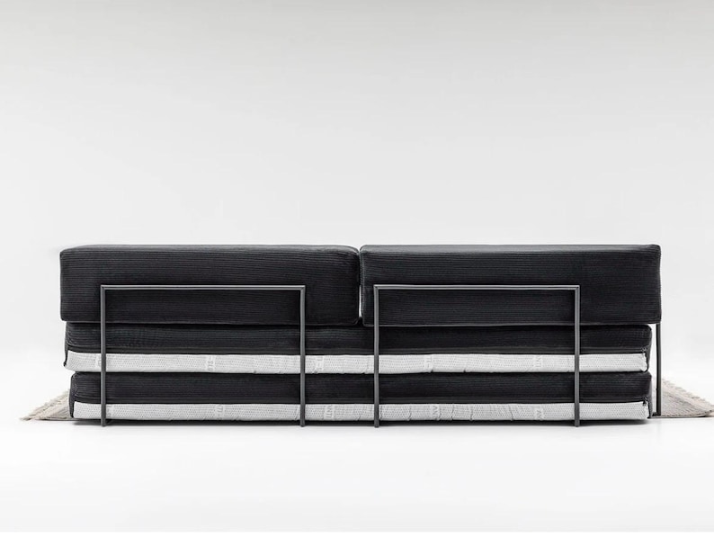 May include: A modern black sofa with a minimalist design. The sofa features a rectangular shape with a dark, textured fabric and a metal frame. The cushions are stacked, with white stripes adding contrast.