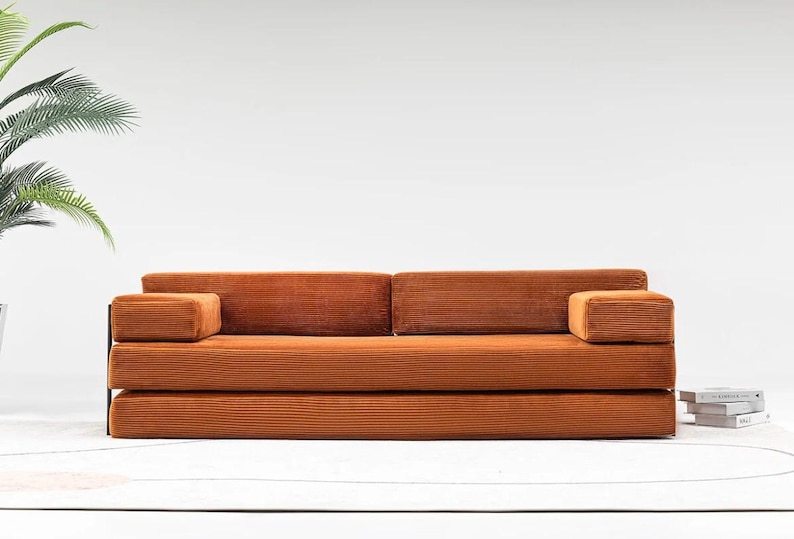 May include: A modern, corduroy-textured sofa in a warm orange hue. The sofa features a low profile with a rectangular shape, including two armrests. The design is minimalist, with a focus on clean lines and a comfortable aesthetic.
