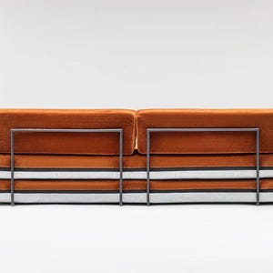 May include: An orange corduroy sofa with a metal frame. The sofa has a stacked design with layers of orange, white, and black fabric. The metal frame is dark gray.