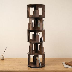 Puede incluir: Una estantería giratoria alta de madera de color marrón oscuro con cinco niveles. Cada nivel presenta un diseño de marco geométrico abierto con divisores verticales que crean múltiples compartimentos de almacenamiento. Varios libros están colocados verticalmente.