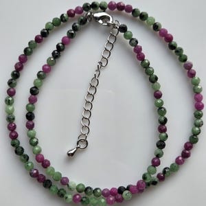 Peut inclure: Un collier de perles composé de petites pierres rondes à facettes dans des tons alternés de magenta vif, de vert forêt et de noir. Le collier comprend un fermoir mousqueton en métal argenté et une chaînette d'extension en métal argenté.