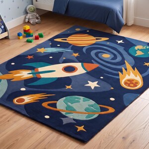 Peut inclure: Un tapis rectangulaire au fond bleu profond orné d'un motif sur le thème de l'espace. Le design comprend une fusée blanche et orange, une planète jaune avec des anneaux, une Terre bleue et verte, une galaxie en spirale et des étoiles.