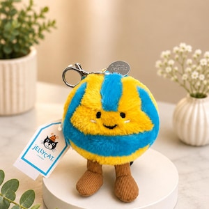 May include: A plush, round keychain toy with a smiling face, featuring yellow and blue stripes. It has brown corduroy legs and a silver keyring. A tag with the text "JELLYCAT LONDON" is attached.