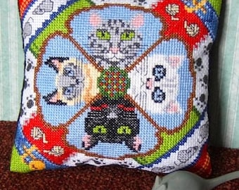 May include: A square pillow with a colorful design featuring four cats with different colored fur. The cats are arranged in a circle with their faces facing outward. The background is a light blue color with white paw prints.