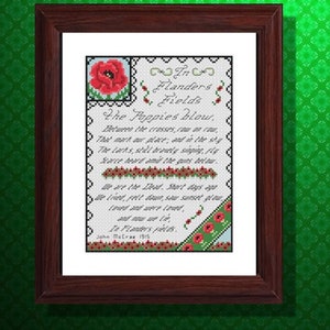 Op de afbeelding: Een ingelijst kruissteekkunstwerk met het gedicht "In Flanders Fields" van John McCrae. Het ontwerp bevat rode klaprozen, groene accenten en de tekst van het gedicht in zwart. De lijst is donkerbruin.