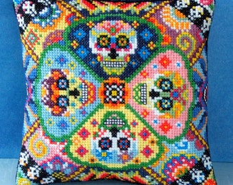 May include: A colorful square pillow with a black background and a repeating pattern of four sugar skulls. The skulls are decorated with bright colors and intricate designs.