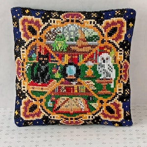 May include: A square, blue and gold cushion with a colourful embroidered design. The design features a black cat, a white owl, books, a crystal ball, and other magical objects.