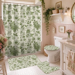 Könnte beinhalten: Ein Set aus Duschvorhang, Toilettendeckelbezug und Badematte mit einem grünen und weißen floralen botanischen Druck. Die Stoffartikel zeigen ein sich wiederholendes Muster aus detaillierten Blumen und Blättern auf hellem cremefarbenem Grund.