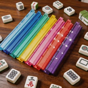 Könnte beinhalten: Eine Sammlung farbenfroher, durchscheinender Mahjong-Spielsteinständer aus Kunststoff in Blau, Grün, Gelb, Rosa, Rot und Lila. Weiße Mahjong-Steine mit verschiedenen Symbolen sind auf einer Holzoberfläche um die Ständer herum angeordnet. Spielsteine für das Spiel Mahjong.