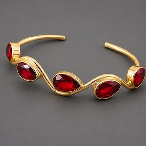 May include: A gold-toned open cuff bracelet featuring a wavy, serpentine metal band set with five faceted, teardrop-shaped red stones. The design alternates the orientation of the stones along the curved frame, creating a continuous, flowing look.