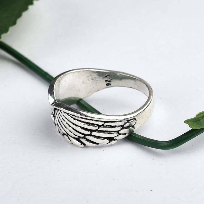 May include: A silver-toned metal ring featuring a detailed wing design with engraved feather textures. The interior of the band is clearly stamped with the hallmark 925, indicating sterling silver composition. The ring has an oxidized finish.
