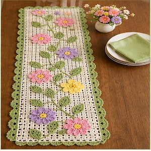 May include: A rectangular crochet table runner featuring an off-white openwork mesh base with a scalloped sage green border. The runner is decorated with a central vine pattern of green leaves and multi-colored flowers in pink, purple, and yellow.
