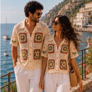 May include: Two matching short-sleeved button-down shirts made of cream-colored crochet fabric. The shirts feature a repeating pattern of square motifs in shades of green, yellow, and rust, along with white daisy flower designs on the sleeves.