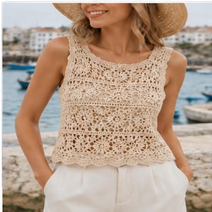 Può includere: Canotta beige all'uncinetto con motivo floreale. Il top senza maniche ha uno scollo tondo e un orlo smerlato. La modella indossa pantaloni bianchi e un cappello di paglia. Lo sfondo mostra una scena costiera con barche ed edifici.