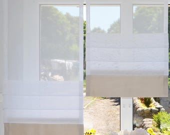 May include: Two white sheer roman shades hanging in a window. Each shade features a horizontal pleated design in the upper section and a solid beige fabric panel at the bottom. The curtains are suspended by vertical white fabric strips at the top.