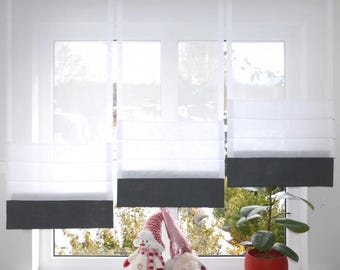 May include: White sheer Roman shades with a dark gray bottom panel are installed over a window. A snowman and a gnome are on the windowsill. A red potted plant is also on the windowsill.