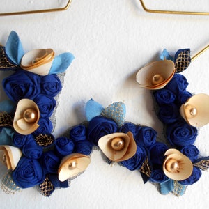 golden metal star decorated with a floral arrangement composed of blue fabric roses, felt leaves, and wooden flowers.
All little flowers and leaves are handmade with high-quality fabric