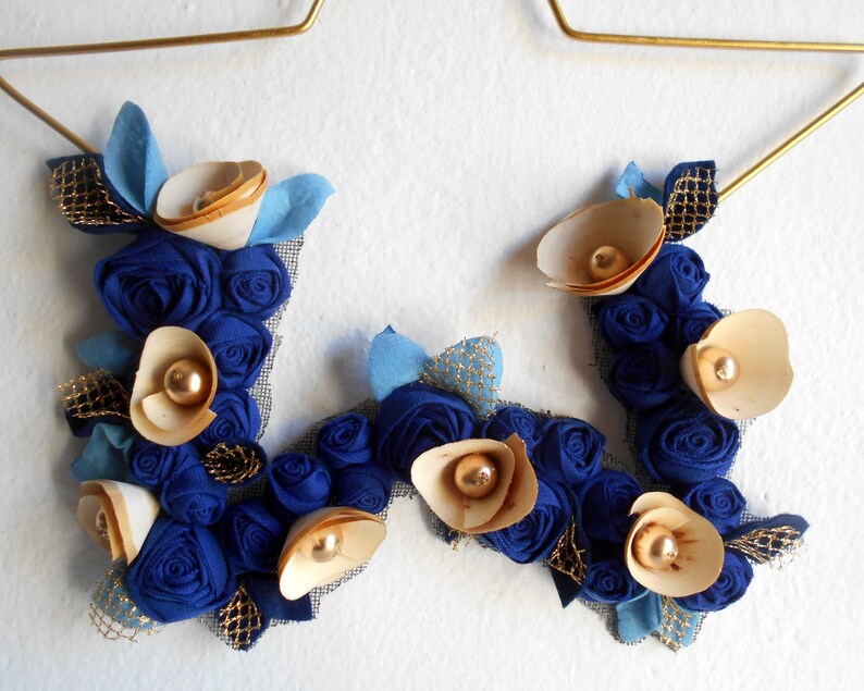 golden metal star decorated with a floral arrangement composed of blue fabric roses, felt leaves, and wooden flowers.
All little flowers and leaves are handmade with high-quality fabric