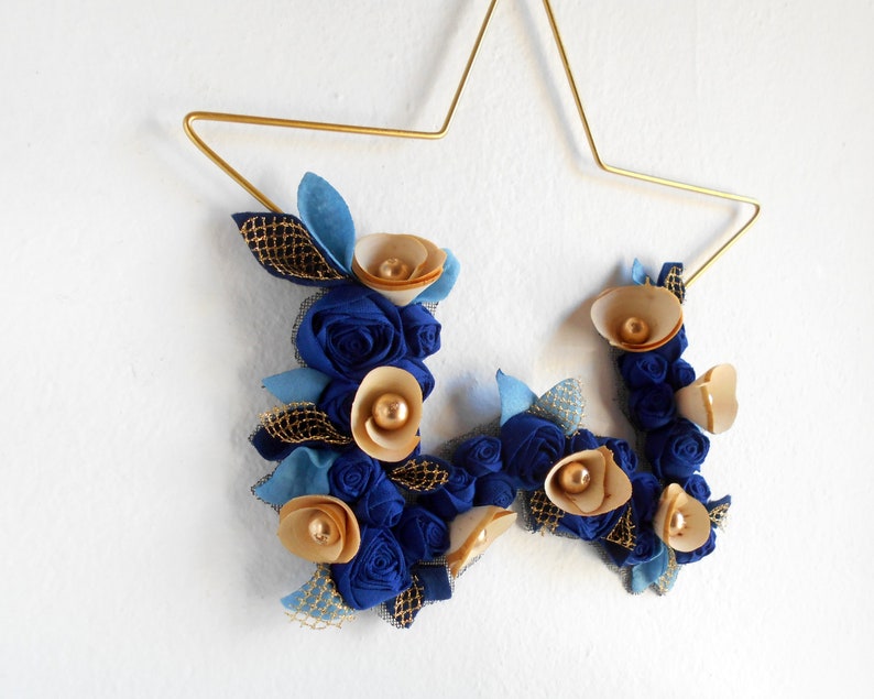 golden metal star decorated with a floral arrangement composed of blue fabric roses, felt leaves, and wooden flowers.

All little flowers and leaves are handmade with high-quality fabric