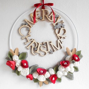 white metal hoop decorated with a floral arrangement composed of blue fabric roses, felt leaves, wooden flowers, and silver details.
A wooden laser-cut MERRY CHRISTMAS SIGN takes place on the top.