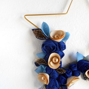 golden metal star decorated with a floral arrangement composed of blue fabric roses, felt leaves, and wooden flowers.

All little flowers and leaves are handmade with high-quality fabric