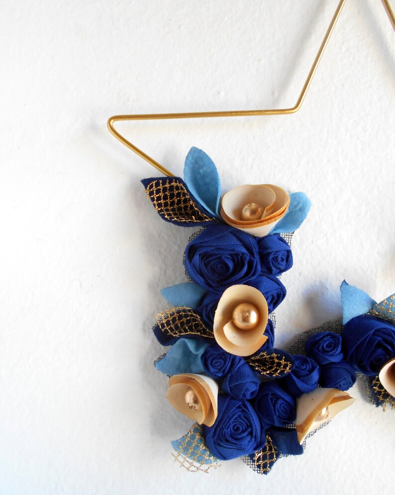 golden metal star decorated with a floral arrangement composed of blue fabric roses, felt leaves, and wooden flowers.

All little flowers and leaves are handmade with high-quality fabric