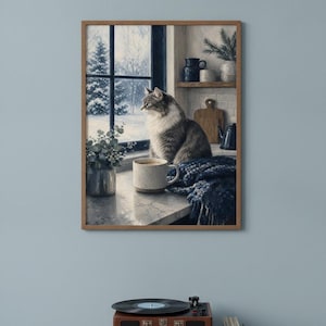 Pode incluir: Uma impressão de arte de parede emoldurada retratando um gato malhado fofo sentado no parapeito de uma janela ao lado de uma caneca de cerâmica, um cobertor de malha azul e uma pequena planta. Pela janela, vê-se uma paisagem nevada com pinheiros.