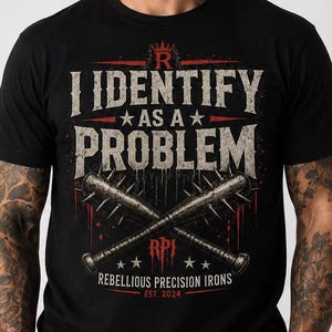 May include: Black t-shirt with the text "I Identify As A Problem" in distressed white font. Features crossed spiked baseball bats and the text "Rebellious Precision Irons Est. 2024".